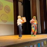 Die Schullleitung und Clown Schnuppe begrüßen die Erstklässler:innen und ihre Eltern in der Aula.