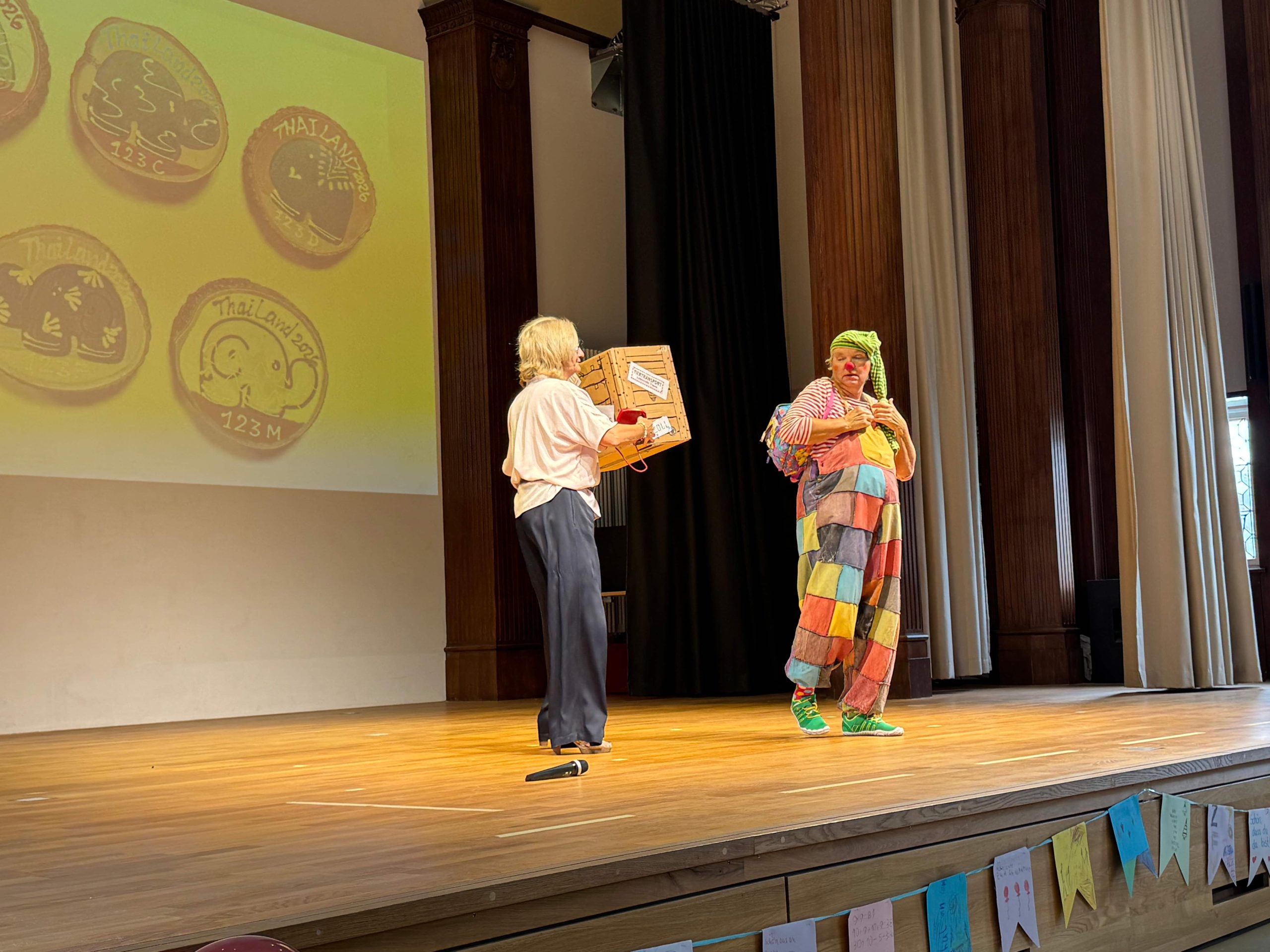 Die Schullleitung und Clown Schnuppe begrüßen die Erstklässler:innen und ihre Eltern in der Aula.